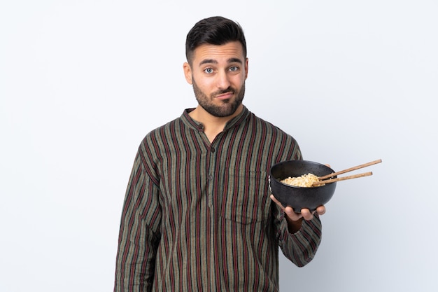 Jeune homme avec une expression triste tout en tenant un bol de nouilles avec des baguettes