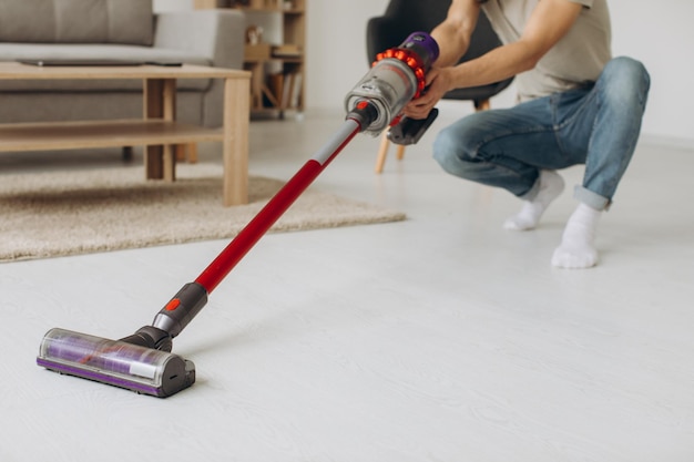 Jeune homme faisant l'aspirateur dans l'appartement