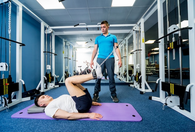 Jeune homme faisant des exercices sur tapis sous la supervision d'un physiothérapeute.