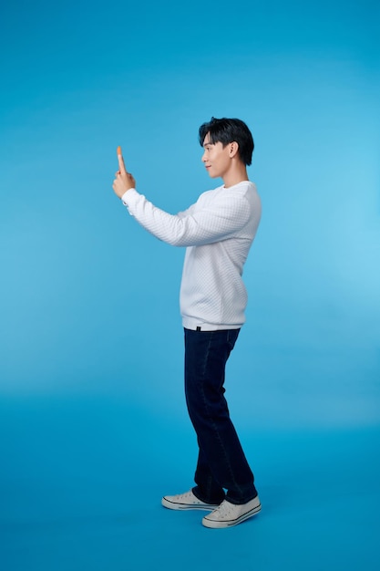 Un jeune homme faisant un selfie sur un téléphone portable isolé sur un fond bleu.