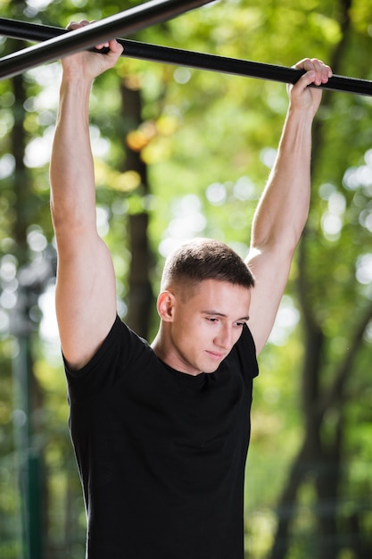 Jeune homme faisant des tractions sur une barre horizontale à l'extérieur, entraînement, concept sportif.