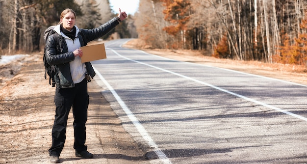 Un jeune homme fait de l'auto-stop à travers le pays. L'homme essaie d'attraper une voiture qui passe pour voyager. L'homme avec le sac à dos est parti en stop vers le sud.