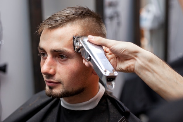Jeune homme fait une coupe de cheveux courte dans un salon de coiffure avec une tondeuse