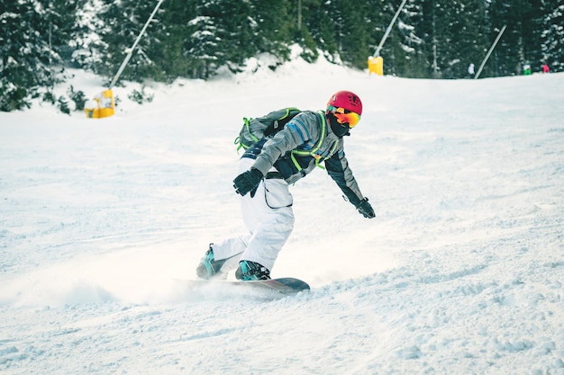 Un jeune homme fait du snowboard et profite d'une journée d'hiver gelée sur les pentes des montagnes.