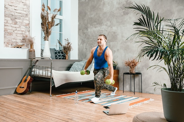 Un jeune homme fait du sport à la maison, entraînement en ligne depuis l'ordinateur portable