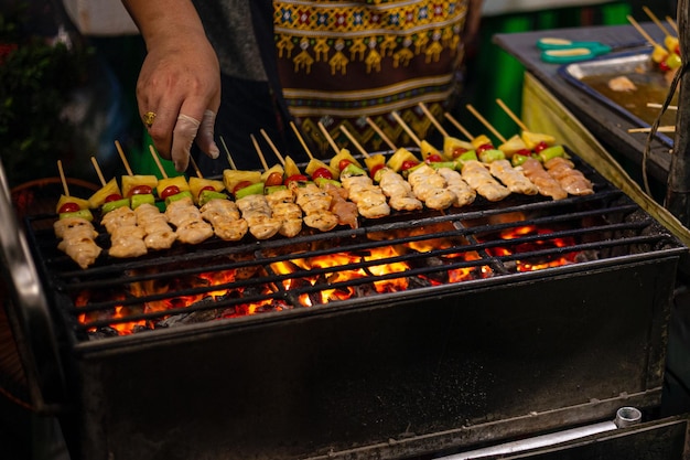 Un jeune homme fait griller une sorte de viande et de légumes marinés sur un gril à gaz pendant l'été