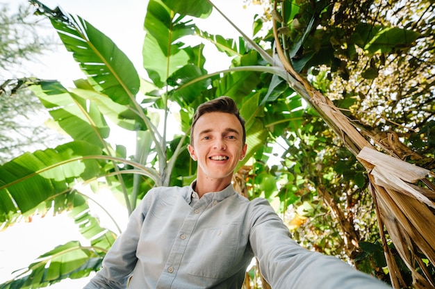 Un jeune homme fait une photo Selfie sur la surface des palmiers bananiers