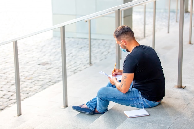 Jeune homme fait ses devoirs sur les marches du campus universitaire