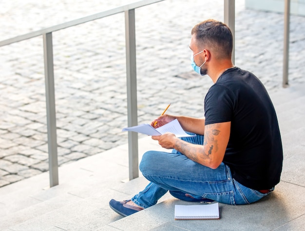 Jeune homme fait ses devoirs sur les marches du campus universitaire