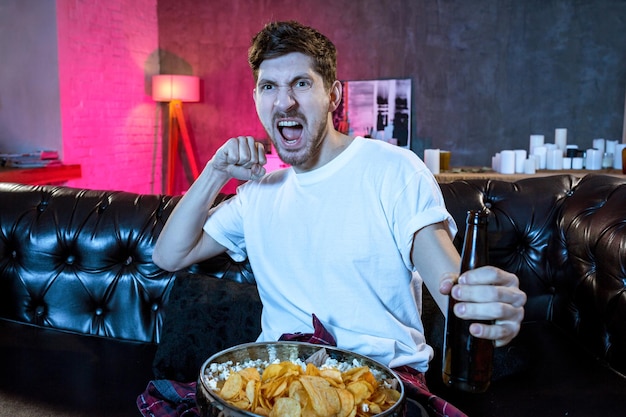 Jeune homme fan regardant un match de football à la télévision célébrant g