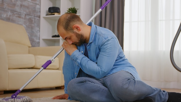 Jeune homme fatigué après avoir nettoyé le sol de la maison avec un détergent.