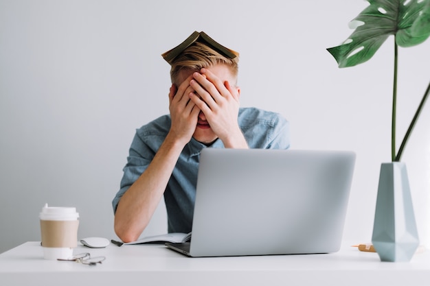 Jeune homme fatigué étudiant étudiant à distance à l'aide d'un ordinateur portable