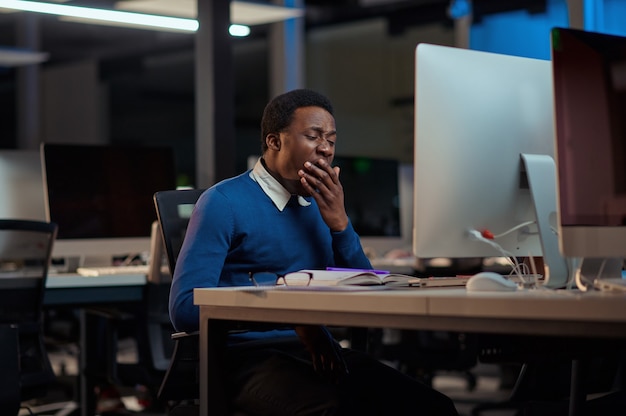 Le jeune homme fatigué travaille dans le bureau de nuit