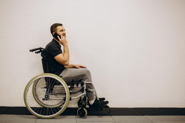 Jeune homme en fauteuil roulant parlant par téléphone portable isolé sur blanc