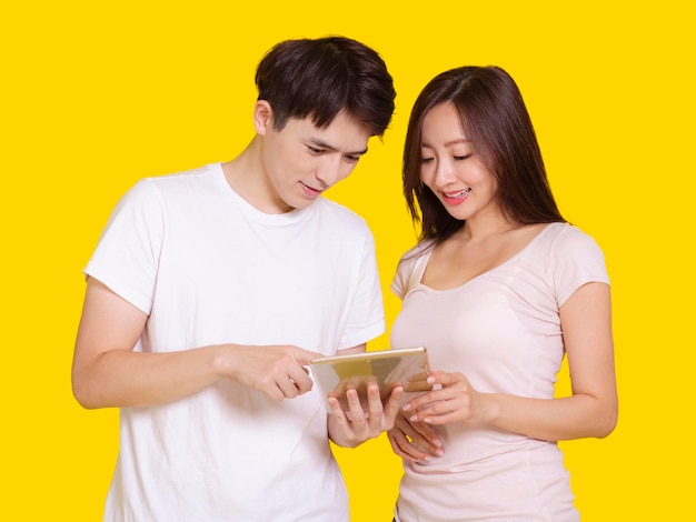 Jeune homme et femme à l'aide d'un ordinateur tabletteIsolé sur fond jaune