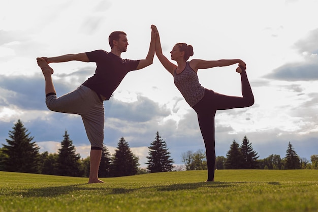 Jeune homme et femme en bonne santé faisant du yoga dans le parc d'été ensoleillé Fitness et mode de vie sain