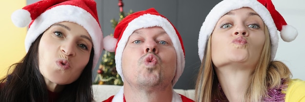 Jeune homme et femme en chapeaux de père noël tenant des verres de champagne et un baiser soufflant