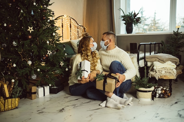 Jeune homme et femme dans des masques se regardant tout en tenant des cadeaux de Noël dans leur chambre