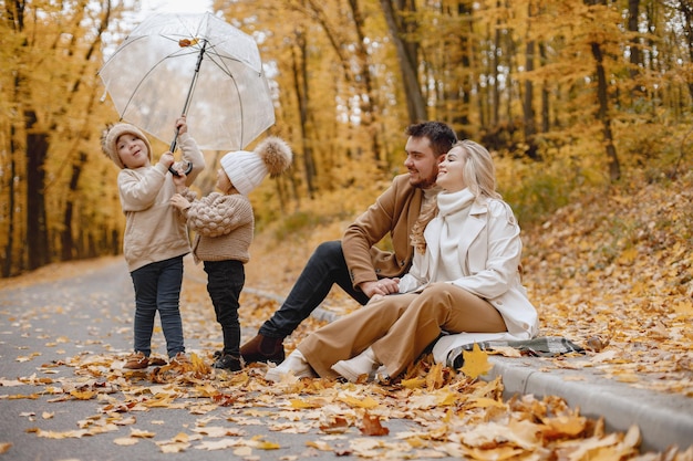 Photo jeune homme, femme et leurs enfants assis dehors dans la forêt d'automne. mère blonde et père brune étreignant. petite fille et garçon tenant un parapluie transparent.