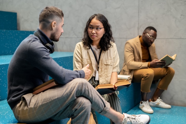 Jeune homme et femme multiculturels avec des livres interagissant à la pause