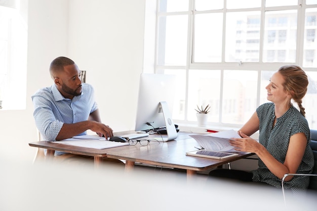 Jeune homme et femme parlant à travers leurs bureaux dans un bureau