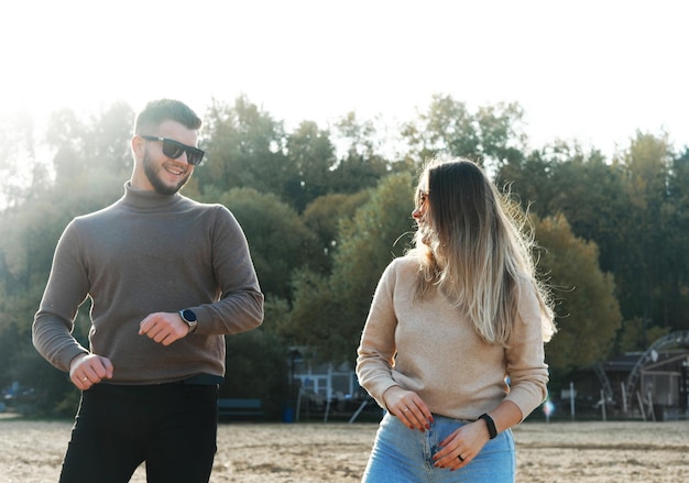 Jeune homme et femme en pull à lunettes de soleil et jeans s'amusent et dansent sur la plage