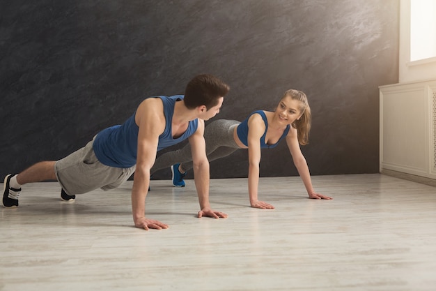 Jeune homme et femme séance d'entraînement au club de remise en forme. Couple de remise en forme faisant des exercices de planche ou de pompes, s'entraînant à l'intérieur, espace de copie