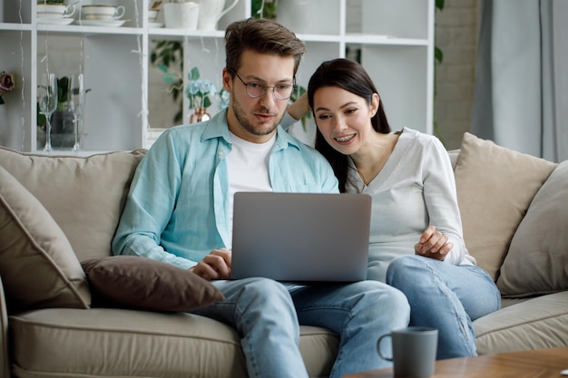 Un jeune homme et une femme sont assis sur le canapé avec un ordinateur portable et rient