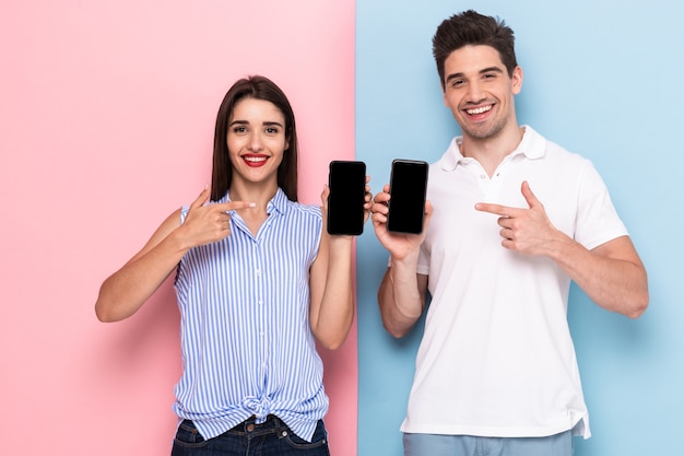 Jeune homme et femme en tenue décontractée tenant les téléphones mobiles ensemble, isolé sur un mur coloré