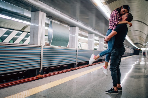 Jeune homme et femme utilisent le métro. Couple dans le métro. Photo gaie de jeune homme tenant la femme dans les mains. Elle sourit. Heureux ensemble. Amour sotry. Vue urbaine moderne souterraine.