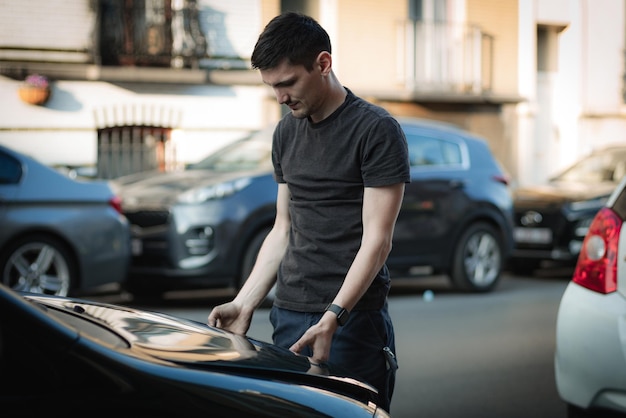 Un jeune homme ferme le capot d'une voiture