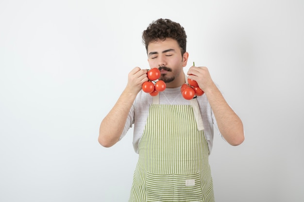 Un jeune homme ferme les yeux et renifle des tomates fraîches biologiques.