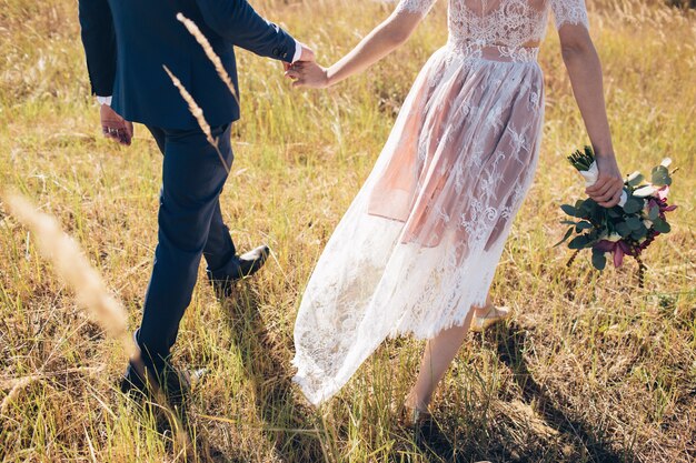 Jeune homme et fille, main dans la main à l'extérieur dans la lumière du coucher du soleil. La mariée et le marié vont se tenir la main. Un couple d'amoureux se promène sur le terrain. le marié dans un costume sombre.