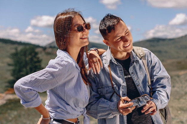 Un jeune homme et une fille se tiennent sur un arrière-plan flou avec une vallée verdoyante. Tenez l'appareil photo dans vos mains et regardez le paysage.