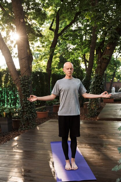Jeune homme de fitness concentré faisant des exercices de yoga méditatif à l'extérieur sur un tapis de fitness