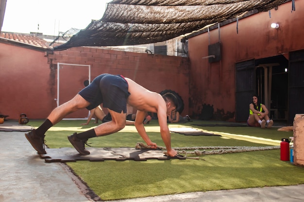 Jeune homme de fitness faisant des pompes à la corde pendant que ses copains se reposent.