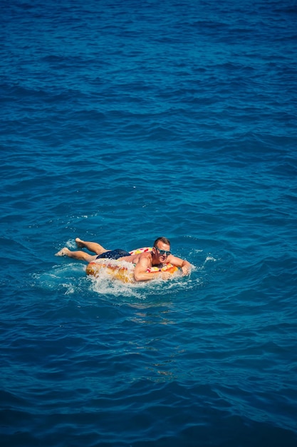 Un jeune homme flotte sur un cercle d'air gonflable dans la mer avec de l'eau bleue Vacances festives par une belle journée ensoleillée