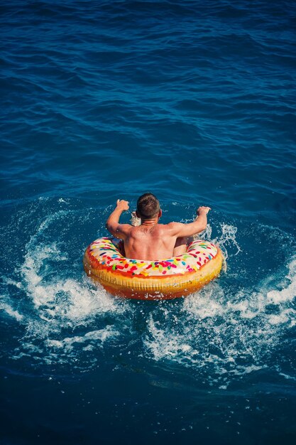 Un jeune homme flotte sur un cercle d'anneau d'air gonflable dans la mer avec de l'eau bleue Vacances festives par une belle journée ensoleillée Vue de dessus du concept de vacances