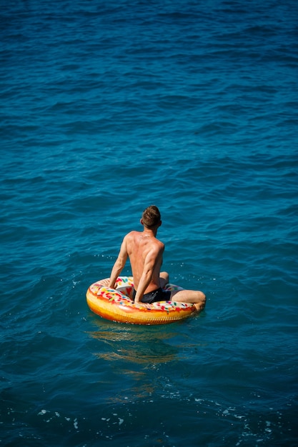 Un jeune homme flotte sur un cercle gonflable d'anneau d'air dans la mer avec de l'eau bleue. Vacances festives par une heureuse journée ensoleillée. Concept de vacances, vue de dessus.