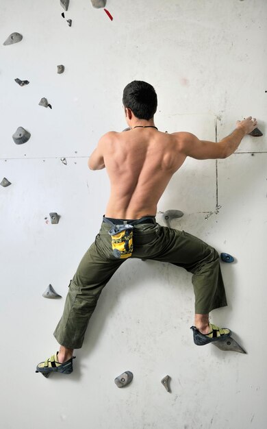 jeune homme en forme faisant de l'escalade libre sur un mur de pratique intérieur