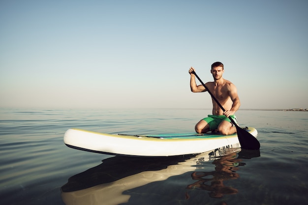 Jeune homme en forme sur paddle board flottant sur le lac