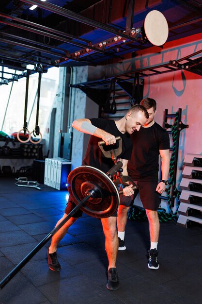 Un jeune homme fort effectue des exercices dans le gymnase sous la supervision d'un entraîneur. Entraînement puissant par un bel homme. Mode de vie sain