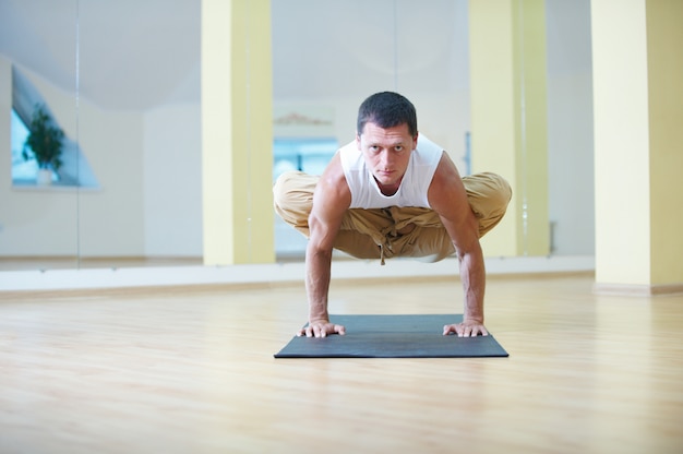 Un jeune homme fort, faire des exercices de yoga. Padma Bakasana Lotus Crane pose dans le studio de yoga