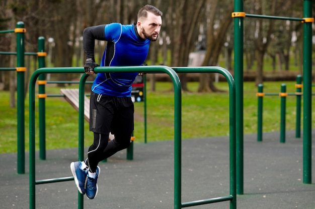 Jeune homme fort faisant les exercices sur les barres asymétriques sur le terrain de sport en été dans la ville