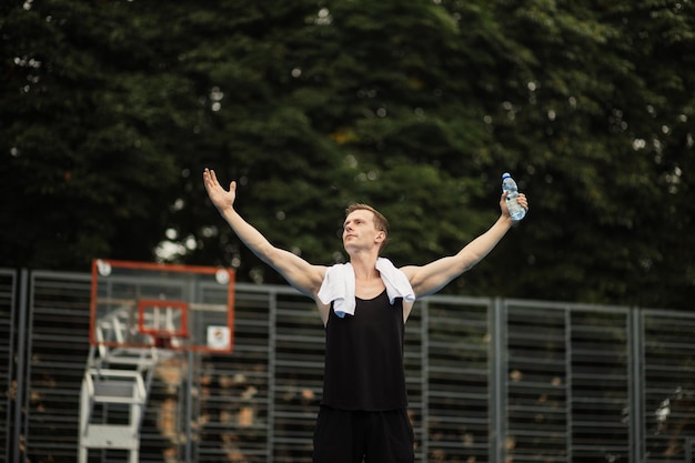 Jeune homme fort avec les mains levées en se tenant debout sur un terrain de basket extérieur