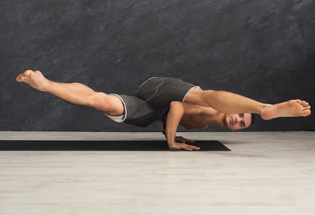 Jeune homme fort pratiquant le yoga, debout dans une pose flexible sur les mains sur un tapis en cours de fitness, faisant des exercices d'équilibre, espace de copie