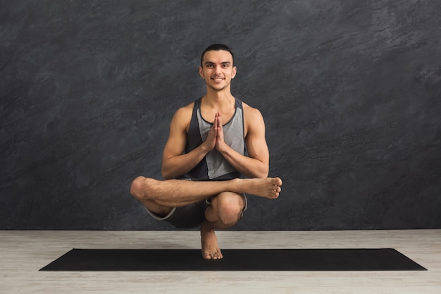 Jeune homme fort pratiquant le yoga, debout dans une pose flexible sur un tapis en cours de fitness, faisant des exercices d'asana, espace de copie