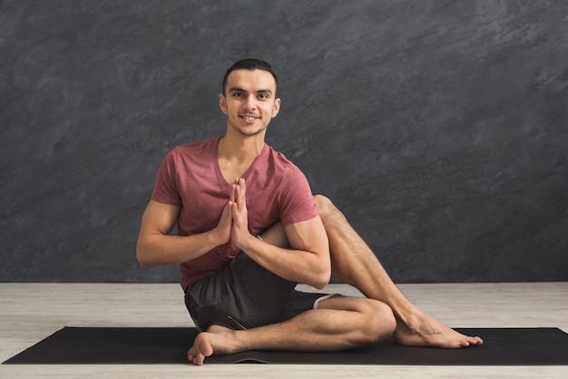 Jeune homme fort pratiquant le yoga, debout dans une pose flexible sur un tapis en cours de fitness, faisant des exercices d'asana, espace de copie