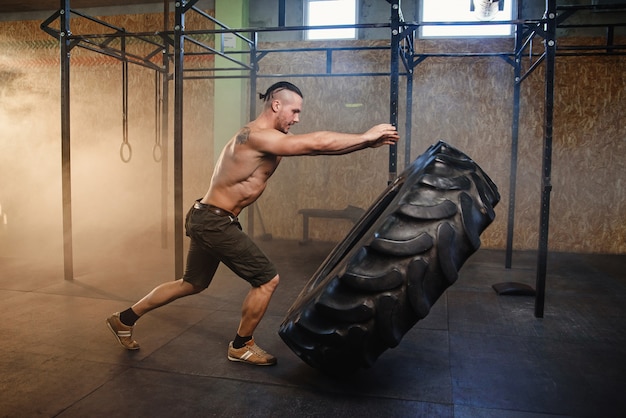 Jeune homme fort, renversant le pneu dans la salle de gym.