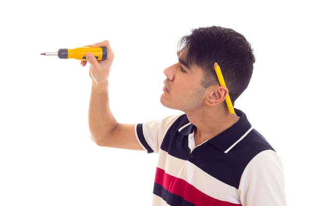 Jeune homme fort en t-shirt blanc et bleu avec un crayon derrière l'oreille tenant un tournevis jaune